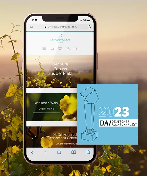 Webshop der Bioweinmanufaktur Schwarztrauber - in Smartphone mit dem Webshop der Bioweinmanufaktur Schwarztrauber, im Hintergrund sieht man das Weingut bei Sonnenuntergang