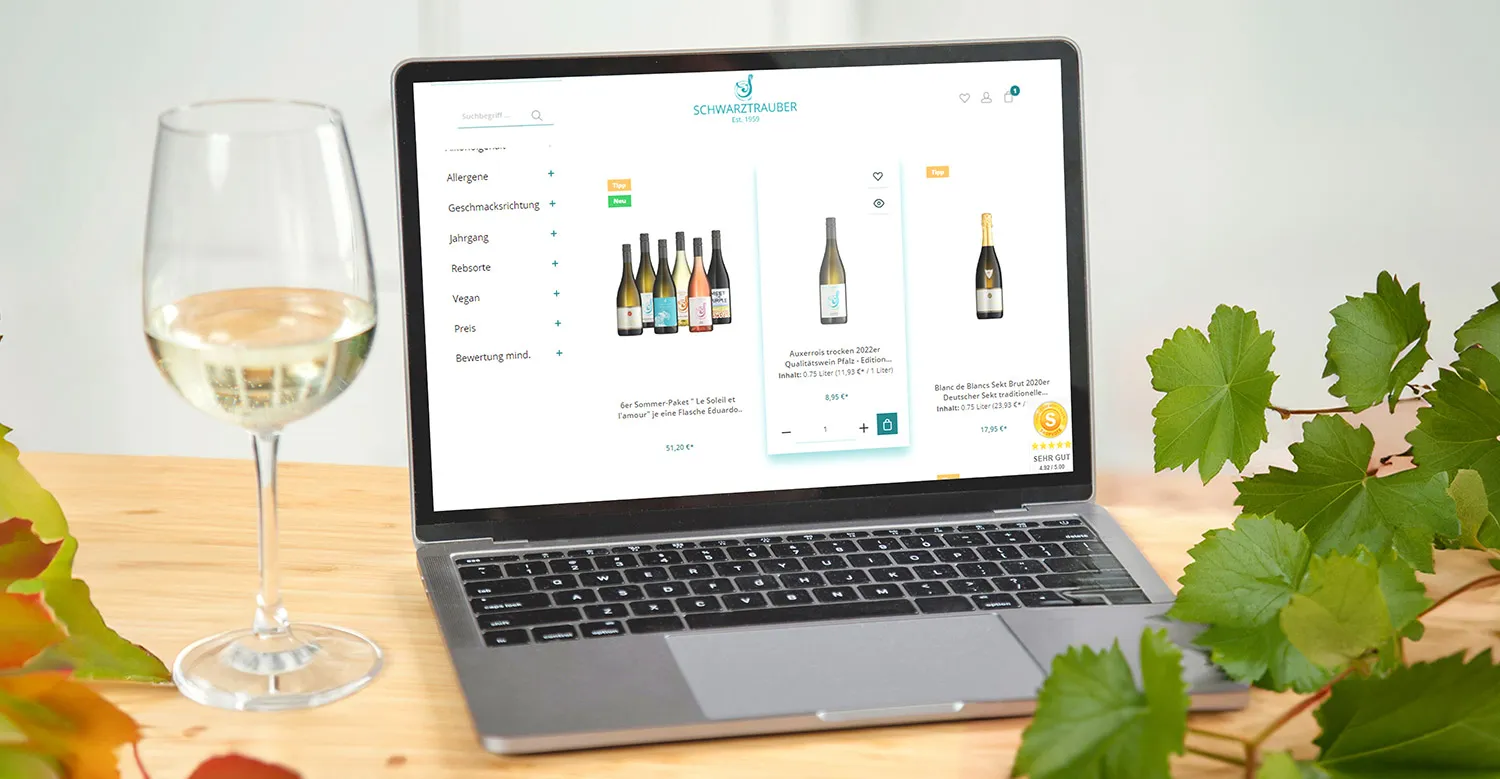 Onlineshop der Bioland Weinmanufaktur Schwarztrauber - ein Laptop auf einem Tisch, der den Onlineshop der Bioland Weinmanufaktur Schwarztrauber zeigt. Daneben steht ein Glas Weißwein.